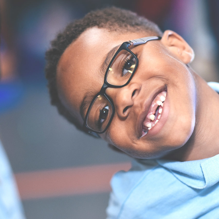 Boy in glasses and missing front teeth smiles at the camera