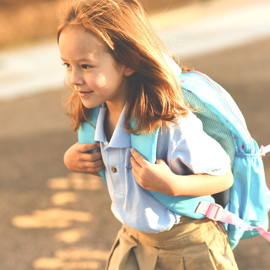 Little girl in uniform and hands on backpack loops walks to school